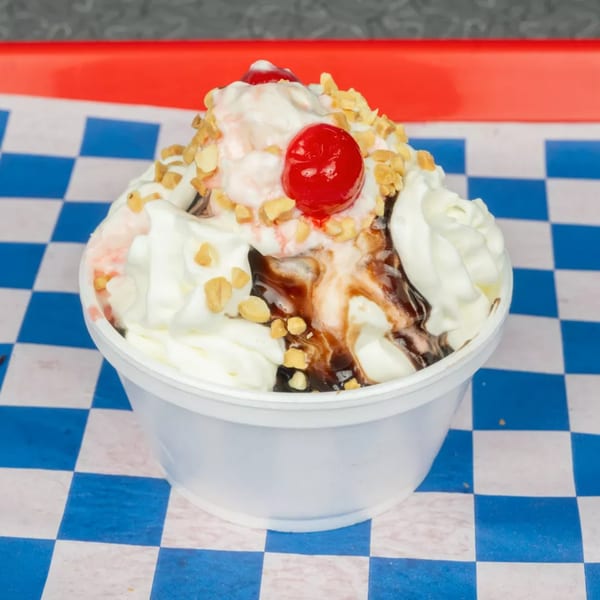 Ice cream sundae with whipped cream, chocolate syrup, nuts, and cherries in a white cup.