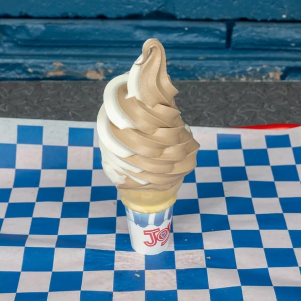 Swirled vanilla and chocolate soft-serve ice cream cone in a paper cup on blue and white checkered paper.