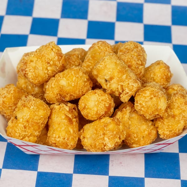 Golden-brown tater tots in a white paper tray with red checkered trim, on a blue and white checkered surface.