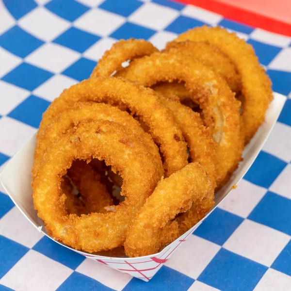 A white paper tray filled with golden-brown onion rings sits on a blue and white checkered surface.