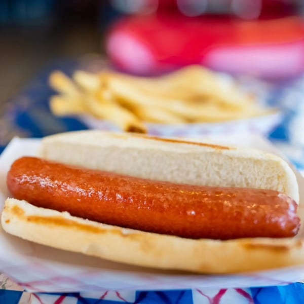 A grilled hot dog in a bun with a side of french fries in a blue and white checkered tray.