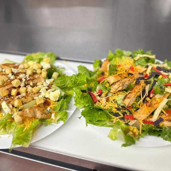 Two fresh salads with grilled chicken, one with croutons and blue cheese, the other with tortilla strips.