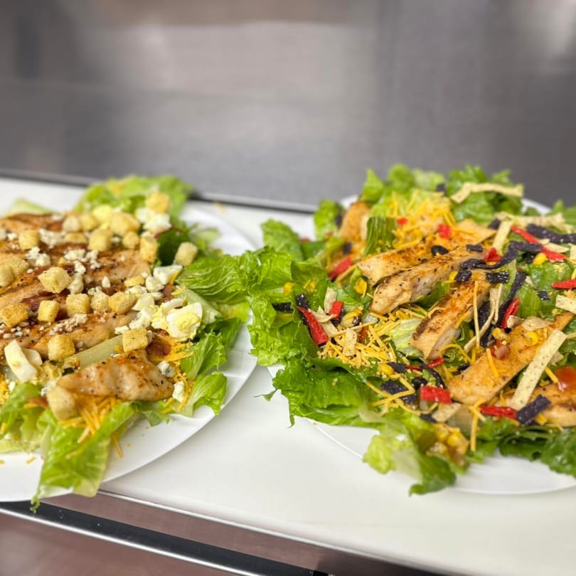 Two fresh salads with grilled chicken, one with croutons and blue cheese, the other with tortilla strips.