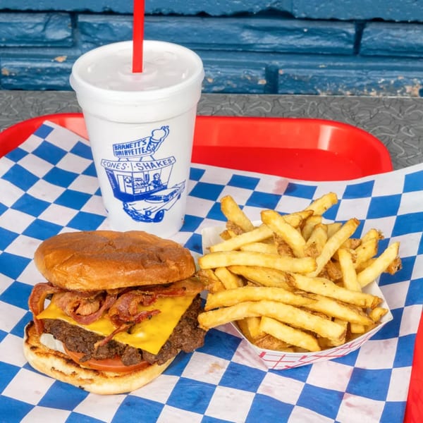 A Barnett's Dairyette bacon cheeseburger, fries, and a drink on a red tray with blue checkered paper.
