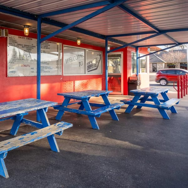 Barnett's Dairyette drive-in with red walls, blue picnic tables, and a menu board under a metal awning.