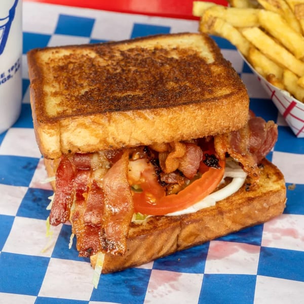 A bacon, lettuce, and tomato sandwich on toasted bread with a side of fries.